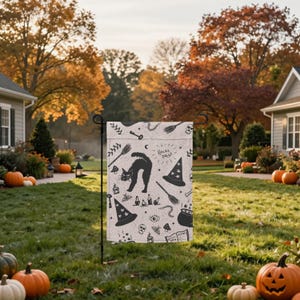 May include: A rectangular garden flag featuring a white background with black illustrations of a black cat, witch hats, brooms, skulls, potions, and the text Hocus Pocus. The flag is displayed on a black metal stand in a grassy yard with pumpkins.