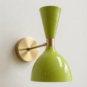 Peut inclure: Une applique murale dotée d'une finition vert citron brillant et d'une forme à double cône. Le luminaire comprend une plaque murale circulaire en laiton, un bras horizontal fin en laiton et un connecteur central en laiton reliant les deux abat-jours coniques vert citron.