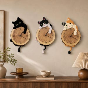 May include: Three wall clocks featuring cat figures in black, black and white, and calico patterns. Each clock face is a circular wood slice with visible grain, black Roman numerals, and clock hands. A cat tail hangs from the bottom of each clock.