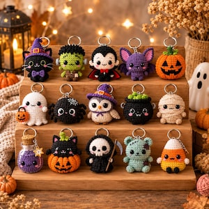 Pode incluir: Uma coleção de quinze porta-chaves de croché com tema de Halloween dispostos num expositor de madeira. As figuras incluem um gato preto, Frankenstein, um vampiro, um morcego, uma abóbora, um fantasma, uma aranha, uma coruja, um caldeirão, uma múmia, uma poção, um gato numa abóbora, a morte, um urso zombie e um doce de milho.