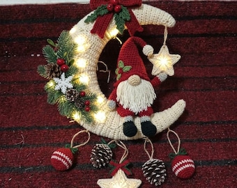 May include: A crocheted crescent moon wall hanging featuring a gnome with a red hat and white beard, decorated with pine branches, pinecones, red berries, a white snowflake, a red bow, and two illuminated crocheted stars.