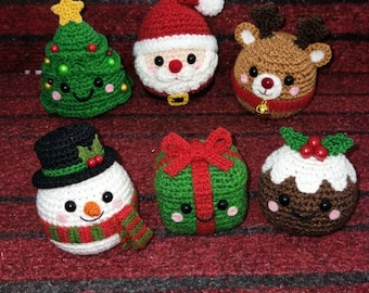 May include: A set of six crocheted Christmas ornaments including a green tree, a Santa Claus, a brown reindeer, a snowman with a black hat, a green gift box with a red bow, and a brown pudding with white icing and red berries.