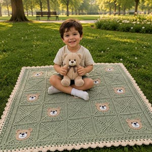 May include: A sage green crocheted blanket featuring a repeating pattern of square panels, each adorned with a small tan teddy bear face appliqué. The blanket is finished with a scalloped cream-colored border and is held by a small teddy bear.