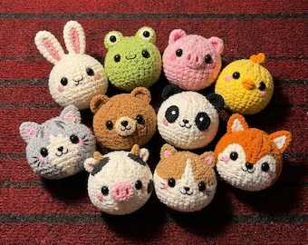 May include: A collection of ten round, crocheted animal plushies including a white rabbit, green frog, pink pig, yellow chick, gray cat, brown bear, panda, cow, calico cat, and orange fox, all featuring black safety eyes and stitched faces.