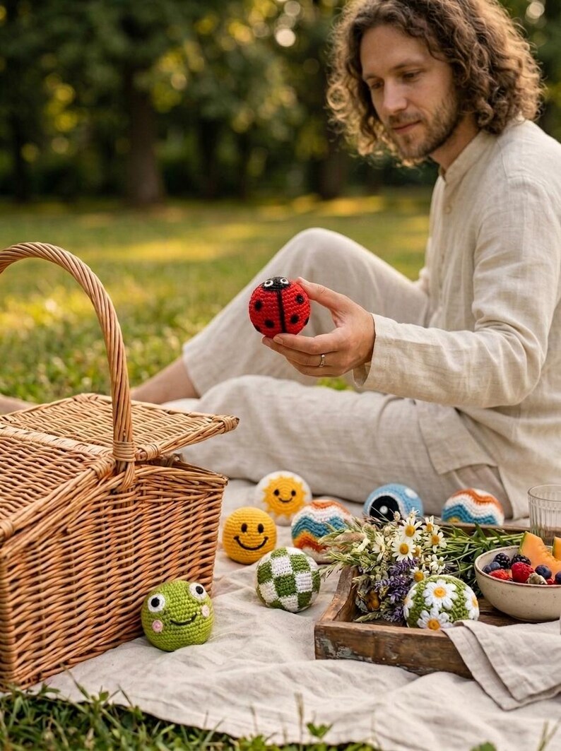 May include: A collection of small, round, crocheted toys featuring various designs including a red ladybug, a yellow smiley face, a green frog, a white and green checkered ball, a sun, a blue yin-yang, and a white ball with daisy flowers.