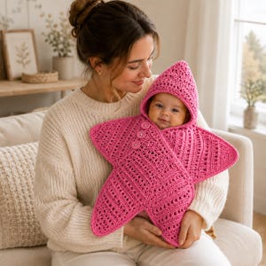 May include: A bright pink crocheted baby swaddle blanket shaped like a five-pointed star with a pointed hood. The garment features a textured, open-stitch pattern and is secured at the front with three matching pink circular buttons.