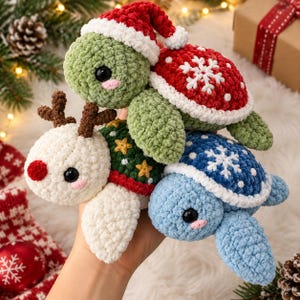 May include: Three crocheted plush toys shaped like turtles. One turtle wears a red and white Santa hat with a red shell featuring a white snowflake. Another turtle has brown reindeer antlers and a red nose. The third turtle has a blue shell with white snowflakes.