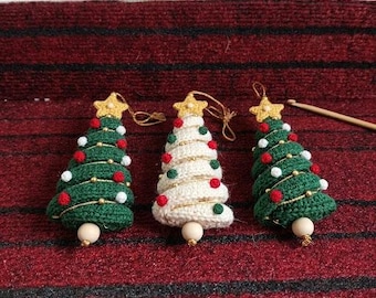 May include: Three crocheted Christmas tree ornaments with two green trees and one white tree. Each tree features a yellow star topper, small red and white pom-poms, gold thread accents, and a single wooden bead at the base with a hanging loop.
