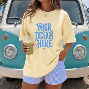 May include: A pale yellow short-sleeve t-shirt featuring the blue text "YOUR DESIGN HERE" in a stylized font with small star accents. The shirt is paired with blue and white vertical striped shorts and a gold chain necklace with a small pendant.