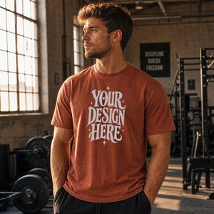 May include: A rust-colored short-sleeve t-shirt featuring white stylized text on the chest that reads "YOUR DESIGN HERE" surrounded by small four-pointed star accents. The shirt has a crew neckline and a standard fit, worn with black shorts.