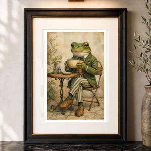 May include: A framed wall art print depicting an anthropomorphic green frog dressed in a dark green blazer, a bow tie, and striped trousers, sitting at a small round table while holding a white teacup. The frog wears brown leather shoes.