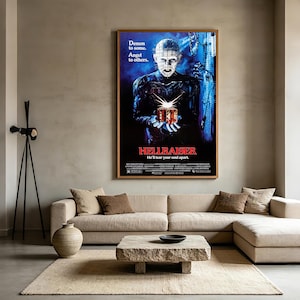 Könnte beinhalten: Ein gerahmtes Hellraiser-Filmplakat mit Pinhead, der eine leuchtende Puzzlebox vor einem dunkelblauen Hintergrund hält. Der Text lautet Demon to some, Angel to others, Hellraiser und He'll tear your soul apart, mit Credits darunter.