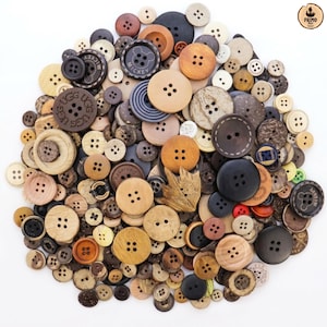 May include: A large collection of assorted buttons in various sizes, shapes, and shades of brown, tan, black, and cream. The buttons are crafted from wood, plastic, and composite materials, featuring two or four holes, some with embossed text like UGG or Mickey.