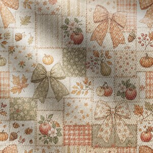 K&ouml;nnte beinhalten: Ein Stoff mit einem Patchwork-Design aus abwechselnden Quadraten mit herbstlichen Mustern. Der Druck zeigt Illustrationen von orangefarbenen K&uuml;rbissen, roten &Auml;pfeln, braunen Eicheln, gr&uuml;nen Bl&auml;ttern und gro&szlig;en Schleifen in Beige, Oliv und Orange.