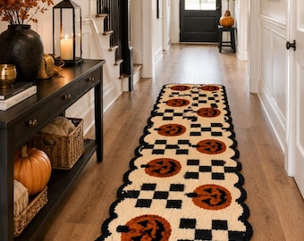 May include: A long, rectangular runner rug featuring a repeating pattern of orange jack-o'-lanterns and black and white checkered squares. The rug has a scalloped edge finished with a thick black border, creating a textured, tufted appearance.