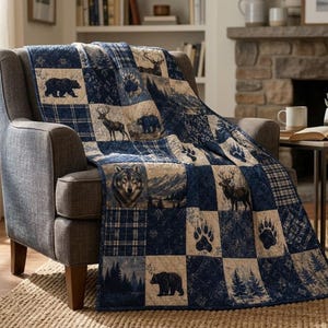Puede incluir: Una colcha de retazos en tonos azul marino y crema con ilustraciones impresas de osos, lobos, ciervos y huellas de patas. La colcha está colocada sobre un sillón tapizado de color gris oscuro, mostrando un patrón repetitivo de motivos animales.