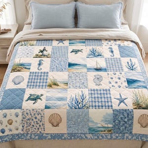 Puede incluir: Una colcha acolchada con un diseño de patchwork de cuadrados azules y blancos. El patrón incluye ilustraciones de conchas marinas, tortugas, caballitos de mar, corales, veleros, faros y paisajes costeros con hierba de playa y olas.