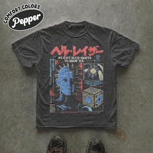 May include: A charcoal gray short-sleeve t-shirt featuring a graphic print of the Hellraiser character Pinhead in blue, alongside a puzzle box illustration, Japanese text, and the English phrases We Have Such Sights To Show You and Hellraiser.