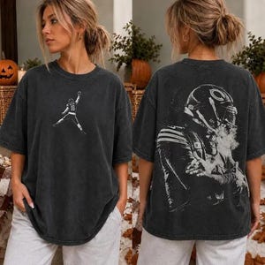 May include: A charcoal gray oversized t-shirt featuring a small white graphic of a football player on the front chest and a large, detailed white graphic of a football player wearing a helmet on the back, both with a distressed, vintage look.