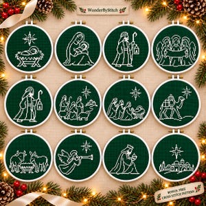 May include: Twelve circular embroidery hoops containing dark green fabric with white cross-stitch designs depicting a nativity scene. Each hoop features a unique religious figure or symbol, including angels, shepherds, a camel, and the holy family.