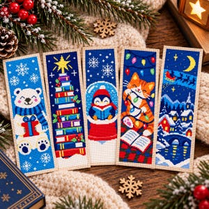 May include: Five rectangular cross-stitch bookmarks featuring holiday themes: a polar bear with a gift, a stack of books as a tree, a penguin in a snow globe, an orange tabby cat with string lights, and a snowy village scene with a sleigh.