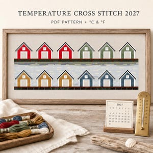 May include: A framed cross stitch pattern titled TEMPERATURE CROSS STITCH 2027 PDF PATTERN °C & °F featuring two rows of small house icons in red, green, yellow, and blue. Includes a 2027 calendar, a gold thermometer, and embroidery floss.