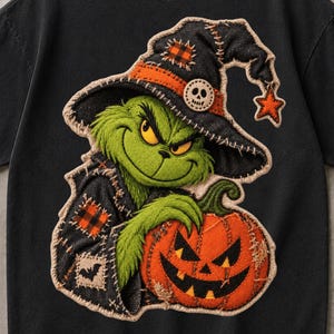 May include: A black short-sleeve t-shirt featuring a large graphic of a green creature wearing a black witch hat with an orange plaid patch and a skull button. The creature holds an orange jack-o'-lantern with a stitched-style design.