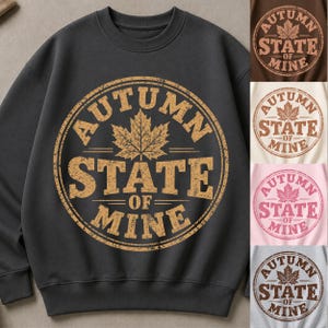 Puede incluir: Una sudadera de cuello redondo gris carbón con un gran gráfico circular de textura desgastada. El diseño incluye una hoja de arce en el centro y el texto "AUTUMN STATE OF MINE" en una fuente negrita y envejecida. Se muestran opciones de otros colores.