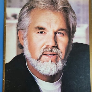 May include: A close-up portrait of a man with a white beard and gray hair. He is wearing a black jacket over a white shirt. The word "front" is printed at the bottom of the image.