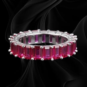 May include: An eternity band ring featuring a continuous row of vibrant, rectangular emerald-cut pink gemstones set in a polished silver-toned metal frame, with each stone secured by small, rounded prongs along the entire circumference.