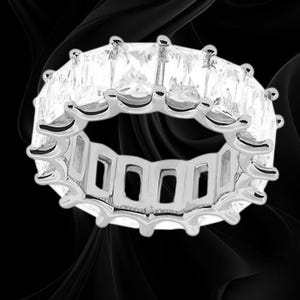 May include: A silver-toned eternity band ring featuring a continuous row of clear, rectangular-cut stones set in a prong setting. The metal band has a polished finish and a series of open rectangular cutouts along the inner circumference of the ring.