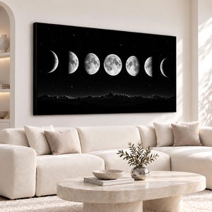 May include: A rectangular wall art print featuring a horizontal sequence of seven moon phases in varying degrees of illumination against a deep black starry sky, positioned above a dark, silhouetted mountain range landscape.