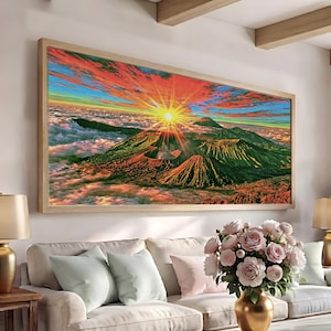 May include: A rectangular wall art print featuring a vibrant sunrise over a volcanic mountain range above a sea of clouds. The sky displays brilliant shades of orange, red, and blue, while the mountains are rendered in deep green and brown tones.