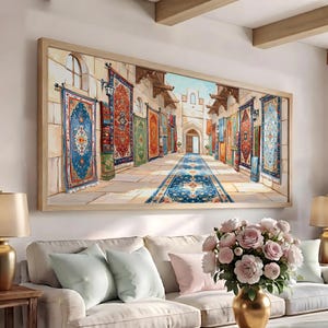 May include: A rectangular framed wall art print depicting a stone alleyway lined with colorful patterned rugs hanging on walls and a long blue runner rug on the floor leading toward a stone archway under a bright blue sky with light clouds.