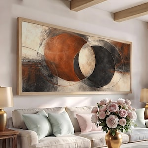 May include: A large rectangular wall art piece in a light wood frame featuring an abstract composition of overlapping circular shapes in shades of burnt orange, charcoal black, and cream, set against a textured, neutral-toned background.