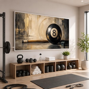 May include: A rectangular wall art piece featuring a black eight ball and a wooden pool cue against an abstract gold and dark gray background. The artwork is framed in white and displayed above a wooden storage unit filled with gym equipment.
