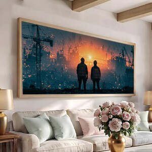 May include: A rectangular wall art print in a light wood frame depicting two figures in high-visibility vests and hard hats standing before a sprawling industrial construction site at sunset, with cranes and glowing orange light filling the horizon.