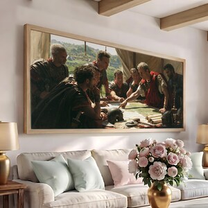 May include: A rectangular framed wall art print depicting a group of Roman soldiers in armour gathered around a table, examining a map. The scene features figures in tunics and cloaks, with a metal helmet resting on the table surface in the foreground.
