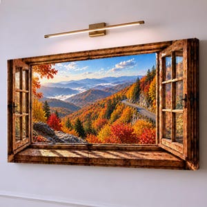 Könnte beinhalten: Ein rechteckiges Wandbild mit einem Fensterrahmen und geöffneten Fensterläden, das eine herbstliche Berglandschaft mit leuchtend orangefarbenem, rotem und gelbem Laub, einer kurvenreichen Straße und einer goldenen LED-Leuchte darüber zeigt.