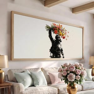 May include: A rectangular wall art piece in a light wood frame featuring a black and white silhouette of a figure wearing a gas mask and holding a large, vibrant bouquet of colorful flowers above their head against a plain white background.
