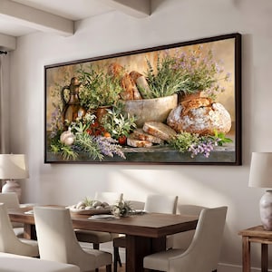 Op de afbeelding: Een rechthoekige wandkunstprint met een rustieke stillevencompositie. De afbeelding toont een oliekruik van donker glas, een groot rond brood met een krokante korst, gesneden brood, verse groene kruiden, takjes paarse lavendel en rode tomaten.
