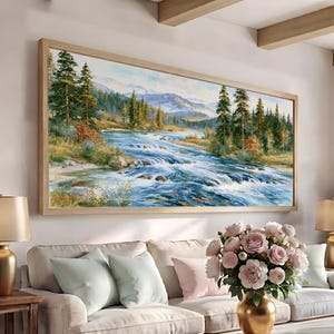 May include: A large rectangular landscape painting in a light wood frame depicting a rushing river flowing through a dense pine forest with distant mountains under a bright sky, showcasing vibrant blue water, green trees, and rocky banks.
