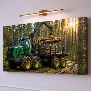 Peut inclure: Un porteur forestier John Deere vert avec de grandes roues à jantes jaunes est garé dans une forêt de pins ensoleillée. La machine dispose d'un bras de grue hydraulique tenant un faisceau de bûches au-dessus d'une remorque chargée de bois.