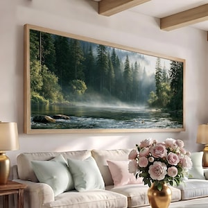Può includere: Una stampa artistica da parete rettangolare con cornice in legno chiaro che raffigura una fitta foresta di conifere lungo un fiume calmo con nebbia mattutina. La scena presenta pini verde scuro e una luce soffusa che riflette sull'acqua.