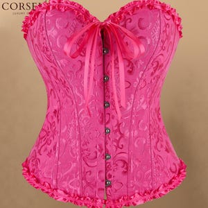 May include: A bright pink corset featuring a tonal damask pattern, a sweetheart neckline with ruffled trim, and a matching ruffled hem. The front closure consists of a vertical row of silver-toned metal clasps and a central pink ribbon tie.