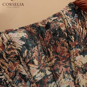 May include: A corset top featuring a woven tapestry pattern in shades of rust, black, gold, and cream. The garment displays vertical boning channels and a structured bodice. The logo for CORSELIA LUXURY CORSETRY is visible in the upper left corner.