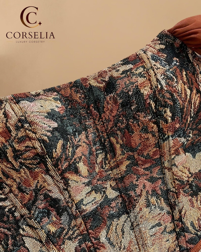May include: A corset top featuring a woven tapestry pattern in shades of rust, black, gold, and cream. The garment displays vertical boning channels and a structured bodice. The logo for CORSELIA LUXURY CORSETRY is visible in the upper left corner.