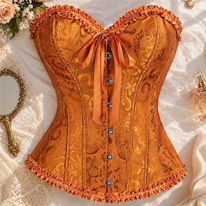 May include: A burnt orange corset featuring a tonal damask pattern, a sweetheart neckline with ruffled trim, a front ribbon tie closure, and a row of silver-toned metal busk clasps. The hem is finished with a matching ruffled orange trim.