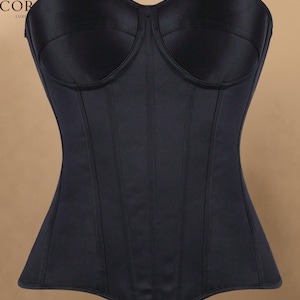 May include: A black strapless corset featuring a sweetheart neckline, vertical seam detailing, and a smooth satin-like finish. The garment displays the text C. CORSET LUXURY in the upper left corner, showcasing a structured, form-fitting design.
