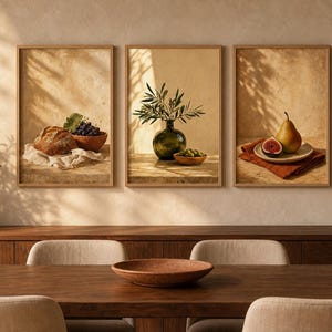 Könnte beinhalten: Ein Set aus drei gerahmten Wandbildern mit Stillleben-Motiven. Das erste zeigt Brot und Weintrauben, das zweite einen Olivenzweig in einer grünen Glasvase und das dritte eine Birne und eine Feige auf einem Teller. Die Bilder haben helle Holzrahmen.